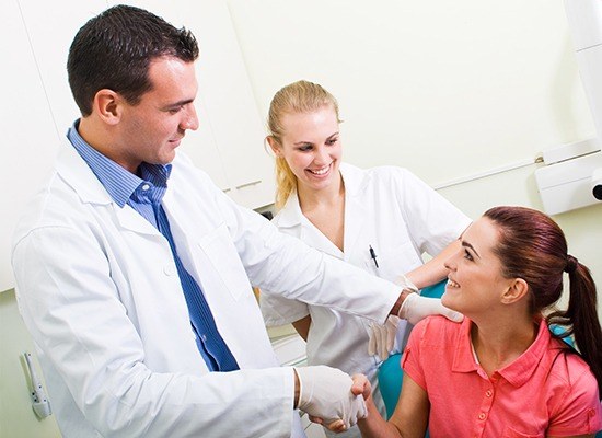 Woman in dental chair shaking dentist's hand