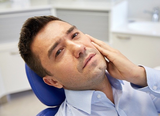 Man in dental chair holding jaw