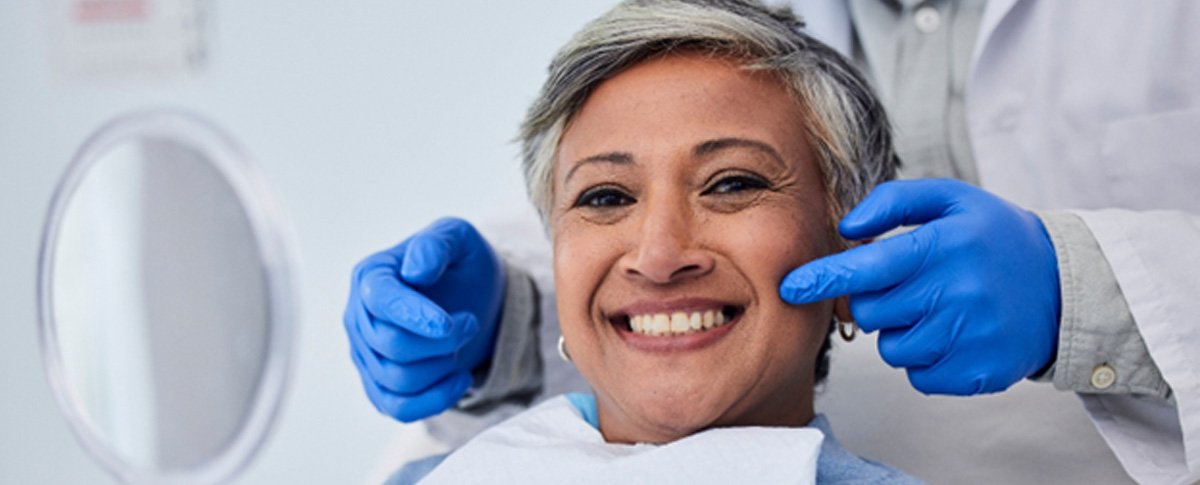 Woman smiling while holding handheld mirror with dentist