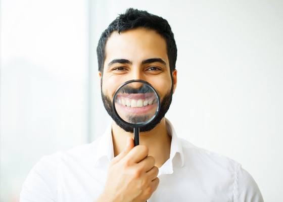 man in white shirt holding magnifying glass to his smile