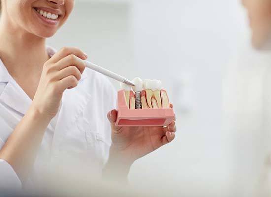 dentist pointing to a model of a dental implant