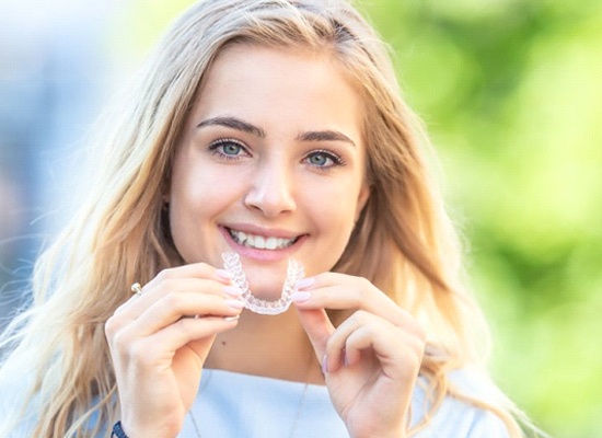 Teen smiling holding Invisalign in Kingwood