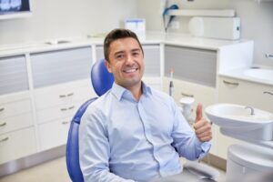 Man at the dentist smiling and holding thumbs up