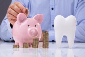 Man putting a coin into a piggy bank next to a tooth model